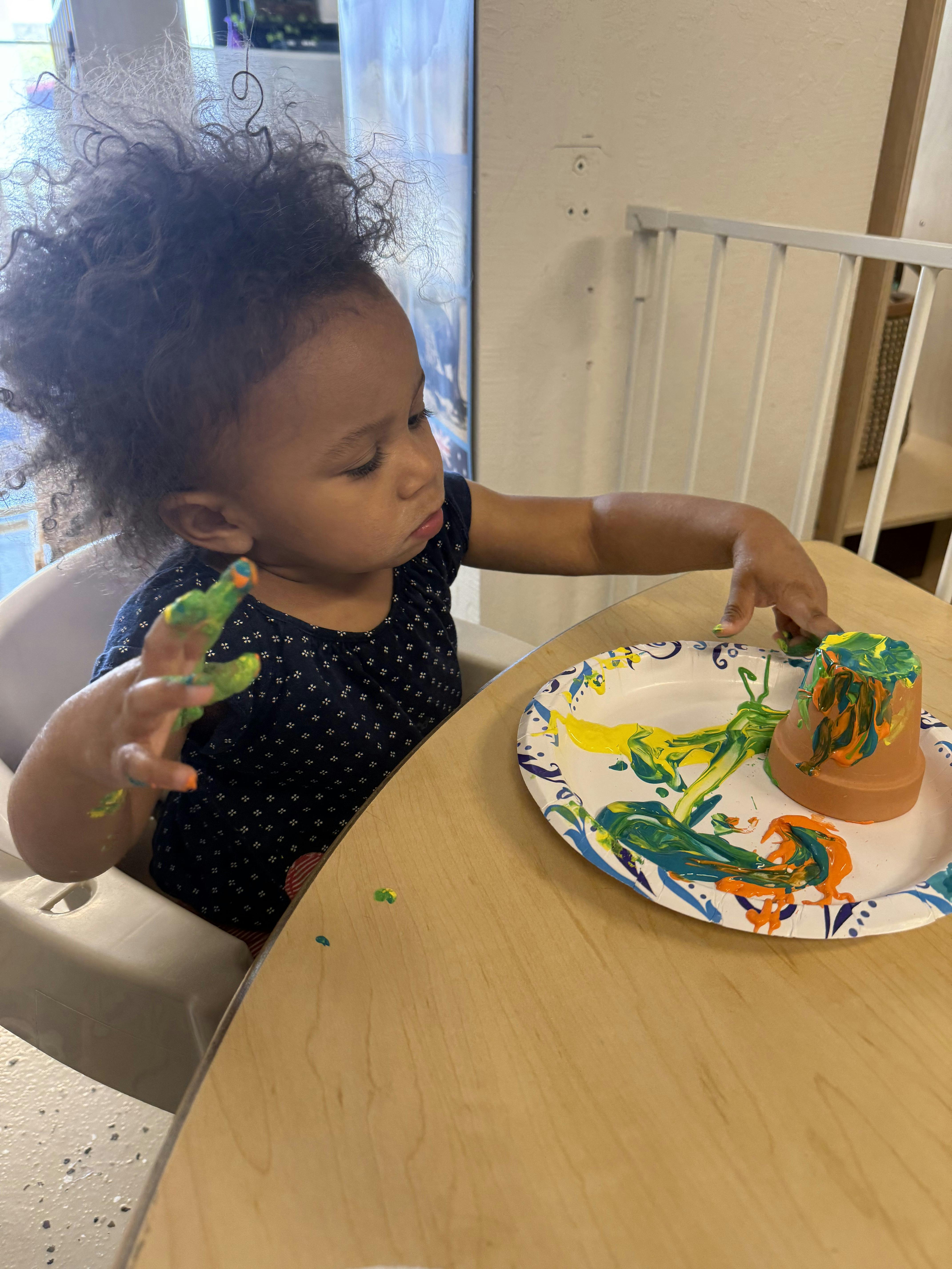Child painting a small pot on a paper plate