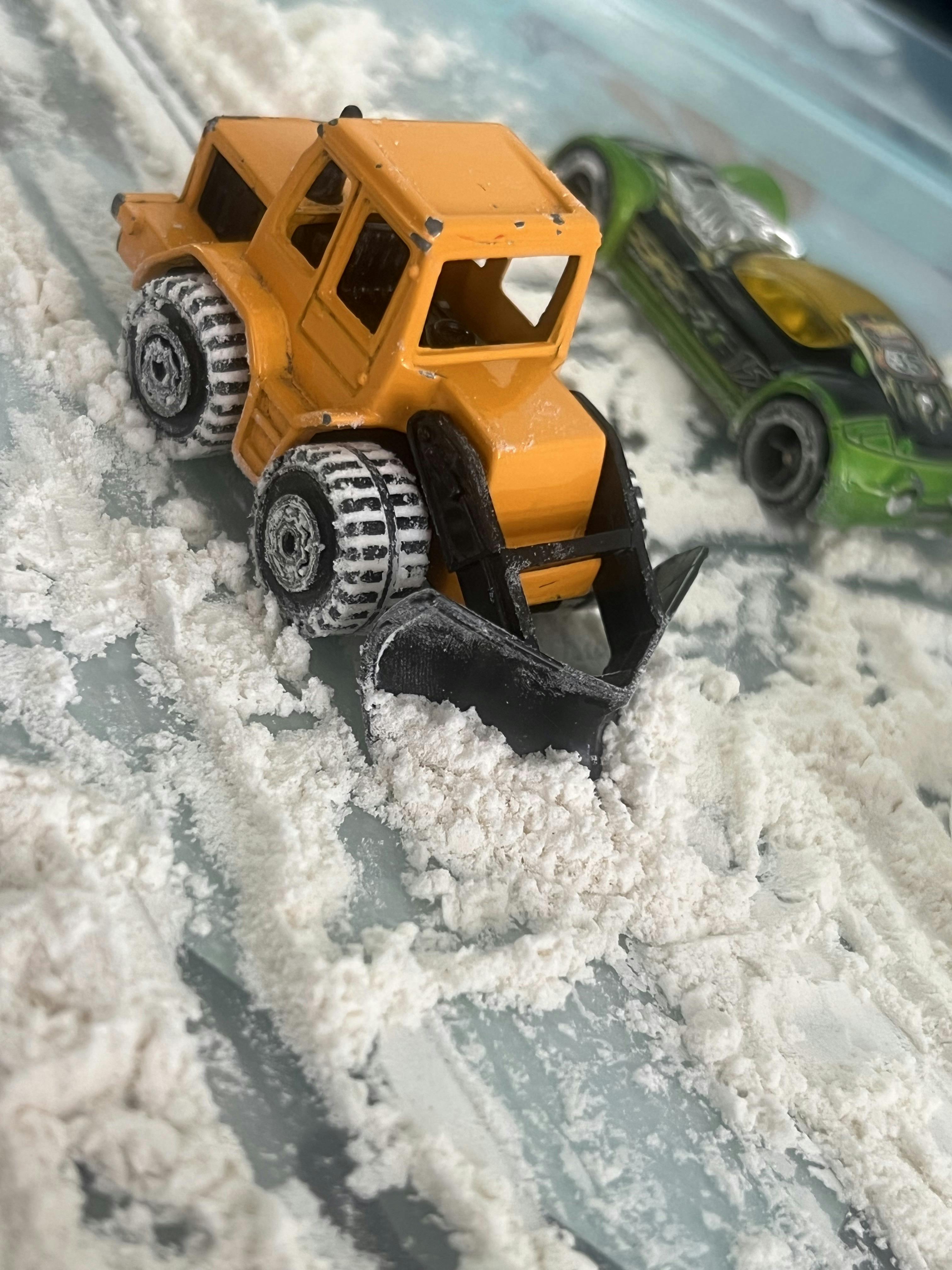 Toy bulldozer pushing white powder with a toy car nearby