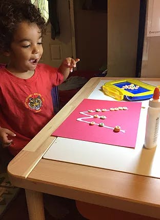 Child pointing at a craft project with cereal pieces on red paper