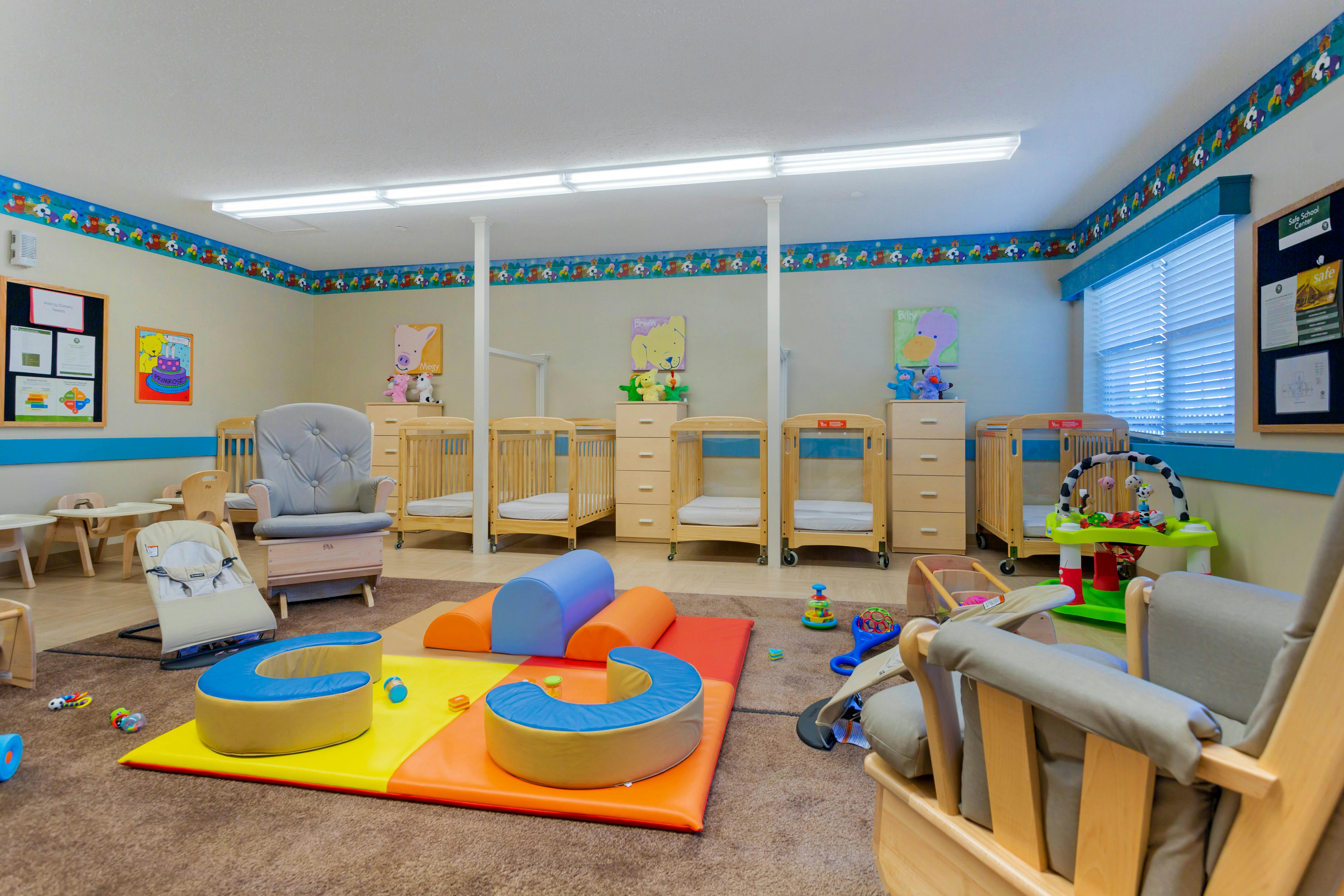 A colorful childcare classroom with cribs, playmats, and chairs