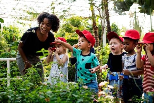 Adult and children in red hats looking at plants in a garden