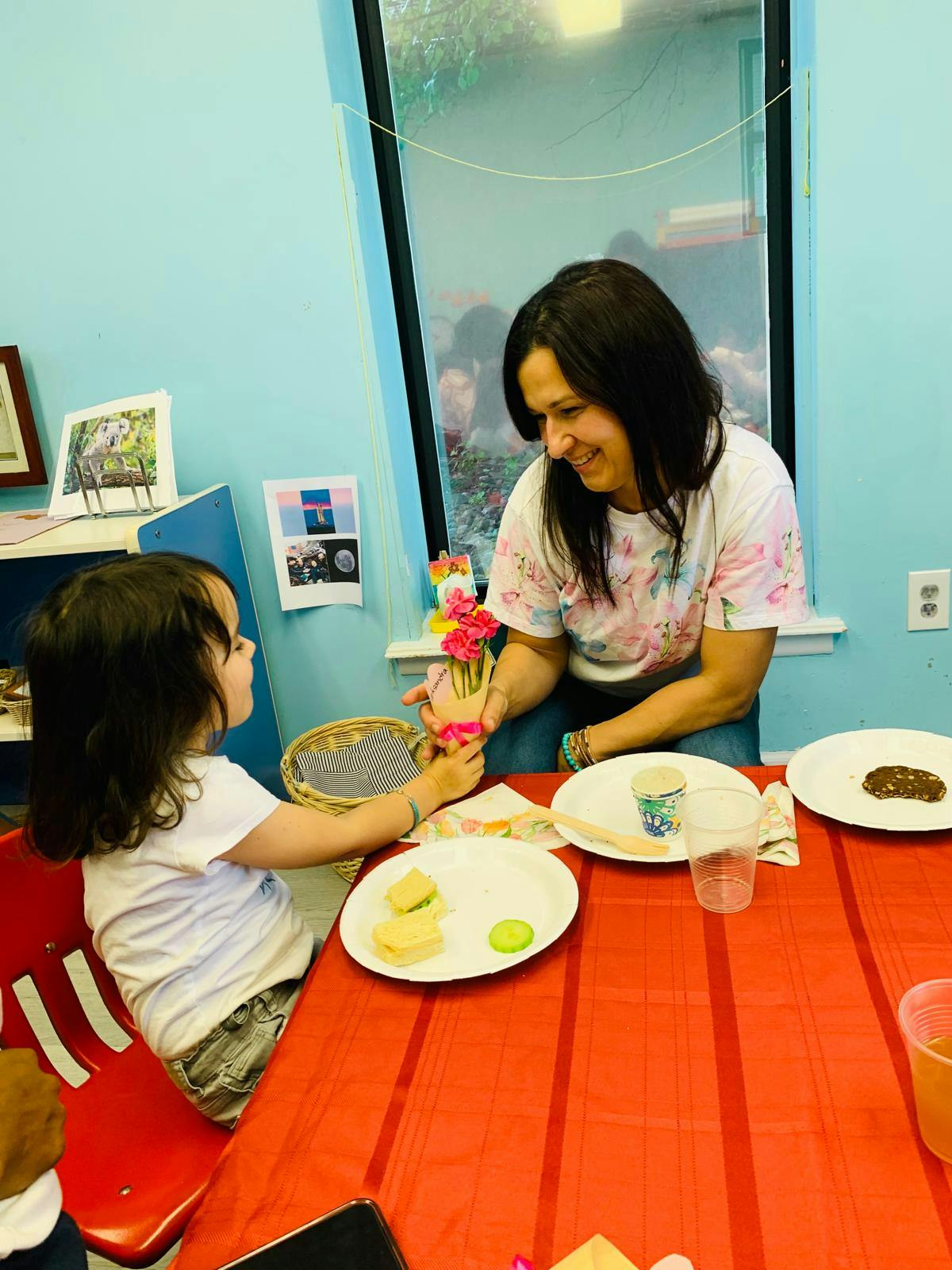 Child handing a small bouquet of pink flowers to a person at a table