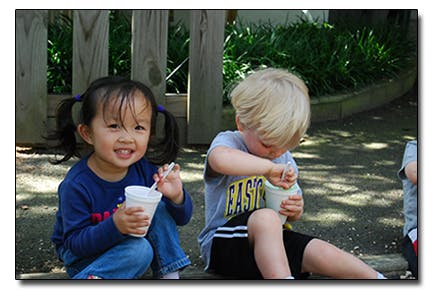 Two children sitting and eating from cups with spoons