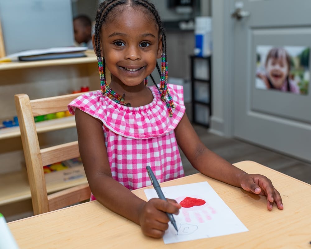 Child drawing a heart on paper at a desk