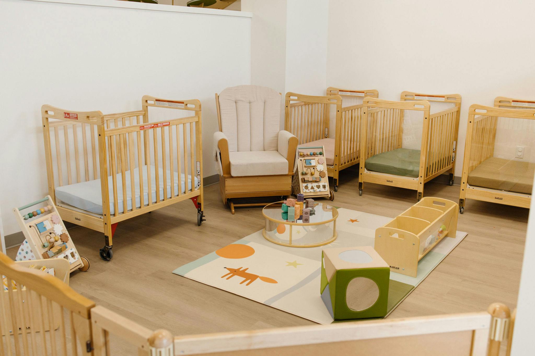 Cribs and child activity area with toys and a play mat in a daycare room
