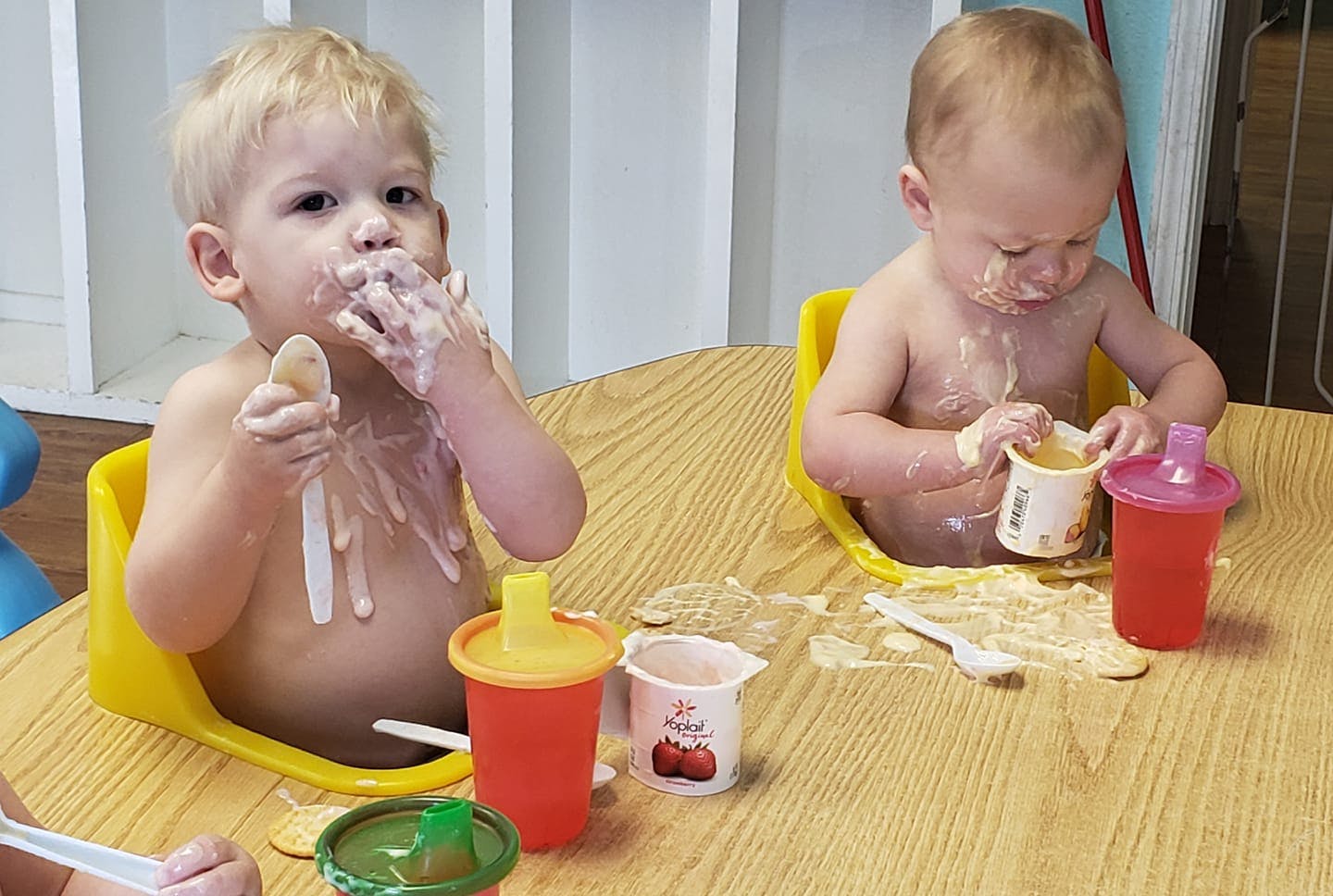 Two children in high chairs eating messy food at a table