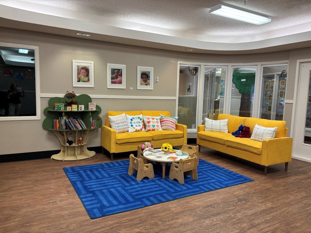 A room with yellow couches, a blue rug, and a tree-shaped bookshelf