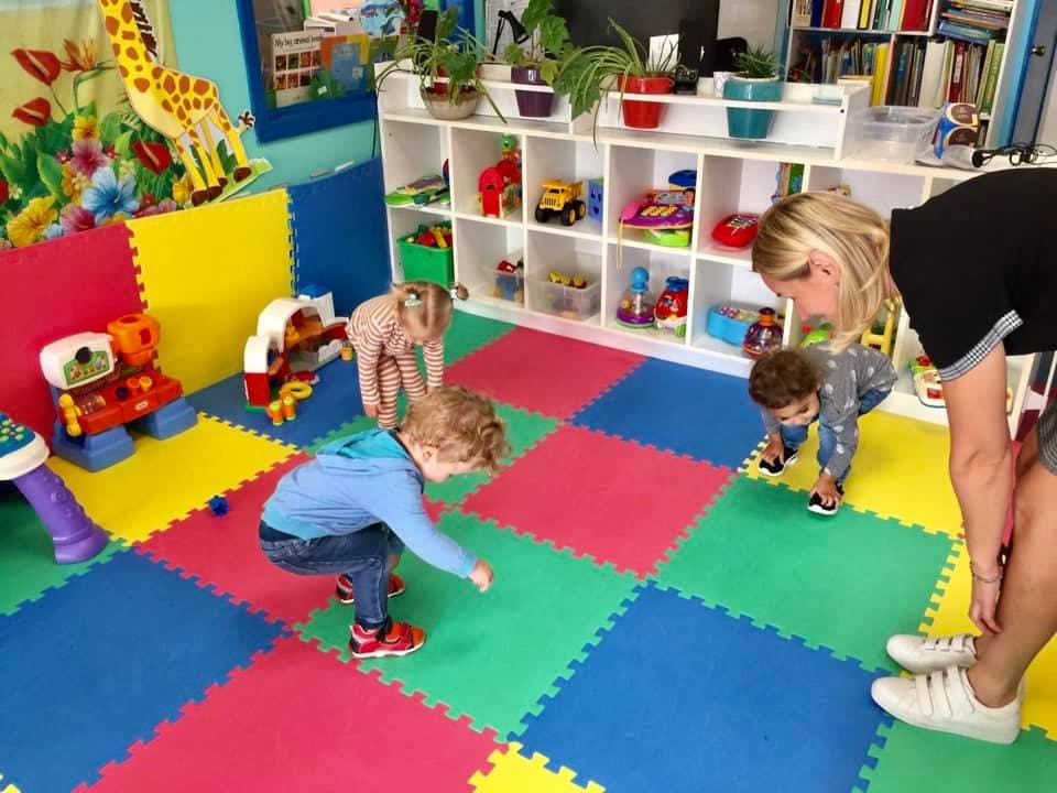 Adults and children playing on a colorful mat in a room with toys