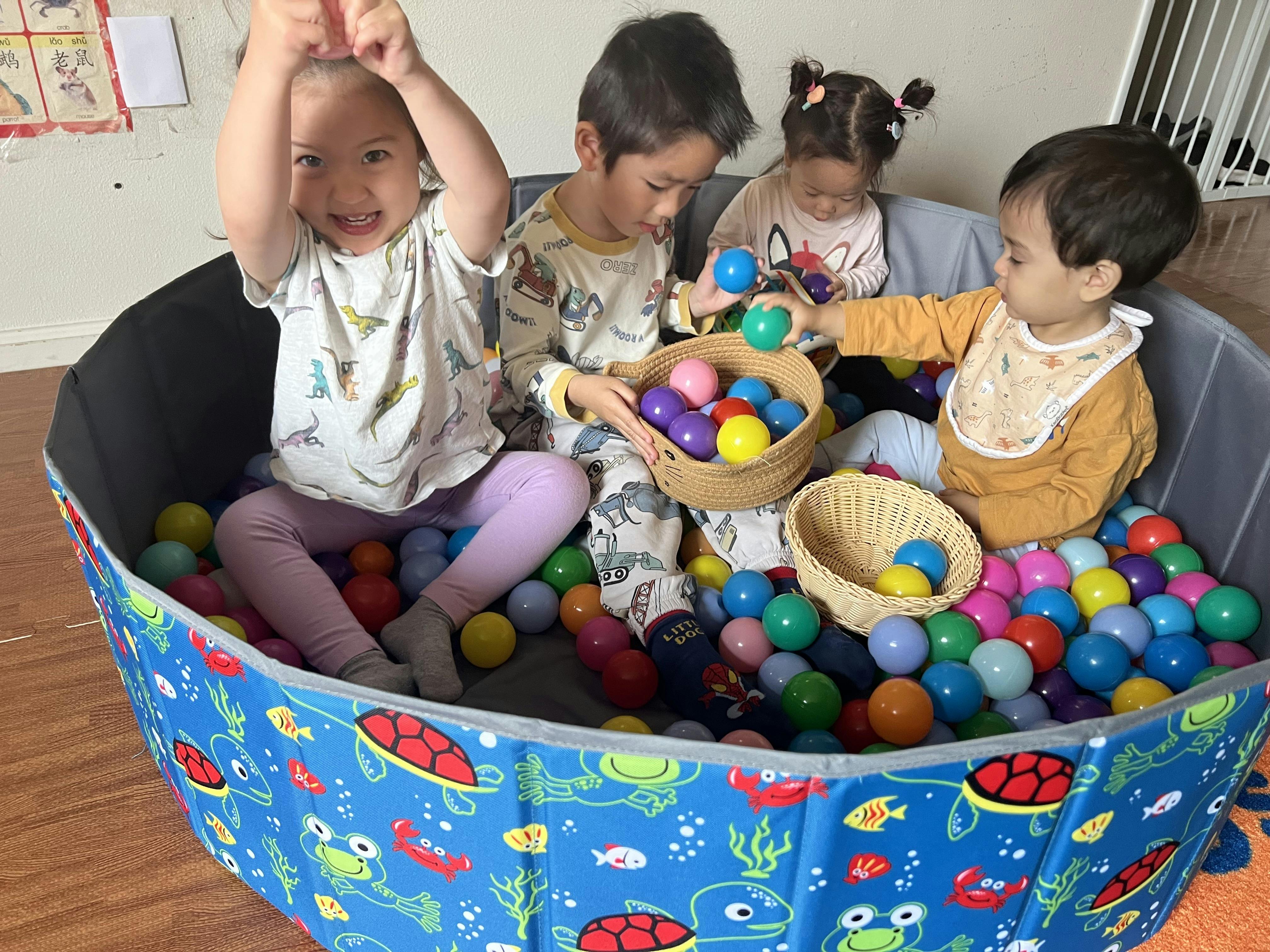 Four children playing with colorful balls inside a foldable ball pit