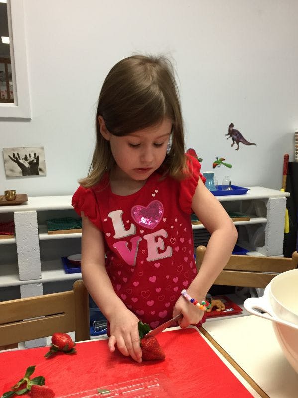 Child cutting a strawberry on a red cutting board