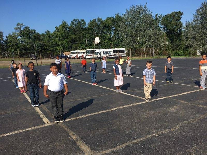 Children standing in marked squares on an asphalt surface