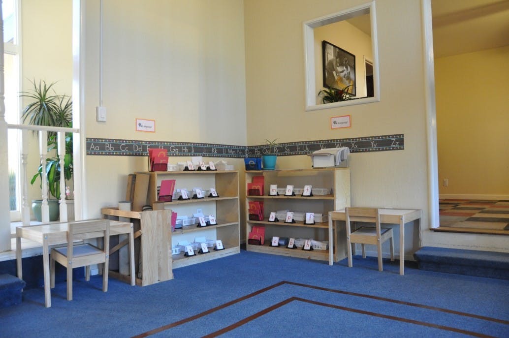 Classroom with small tables and chairs, shelves with learning materials