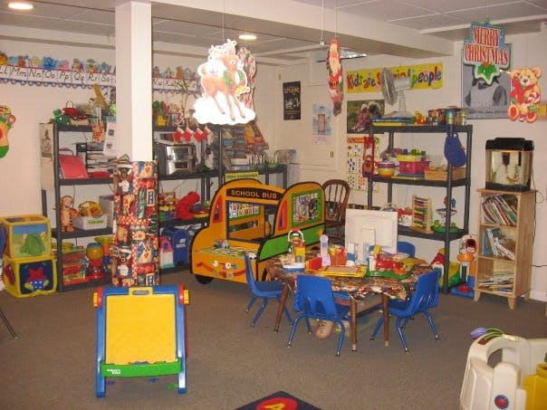 Playroom with small tables and chairs, toy bus, shelves with toys