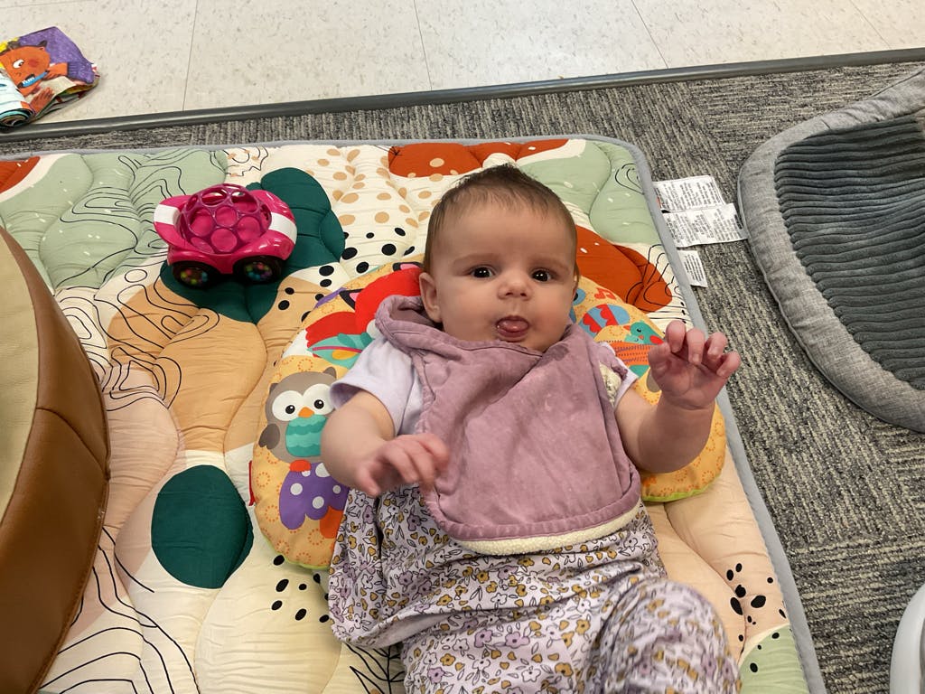 Baby lying on a colorful play mat sticking tongue out