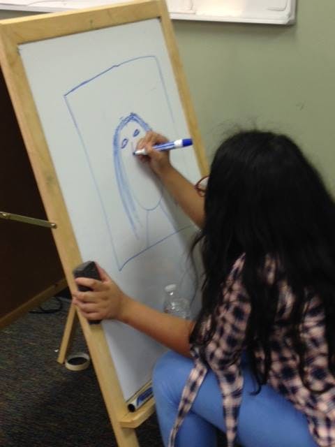 Person drawing a face on a whiteboard with a blue marker