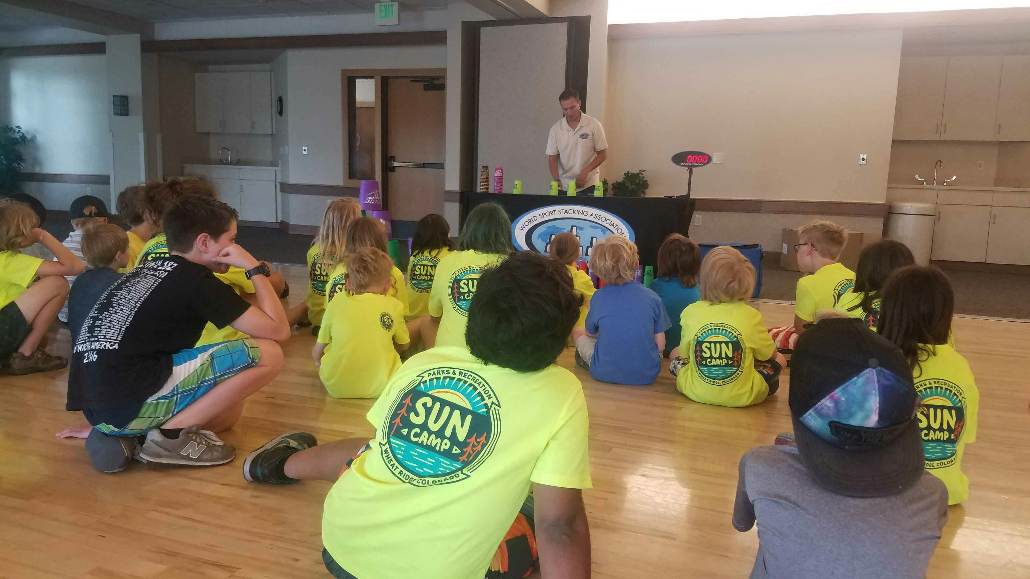 Children sitting on the floor watching a person standing behind a table