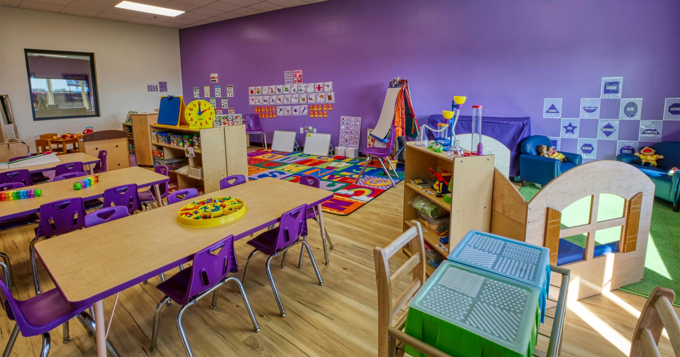 Classroom with purple walls, tables, chairs, and colorful play areas
