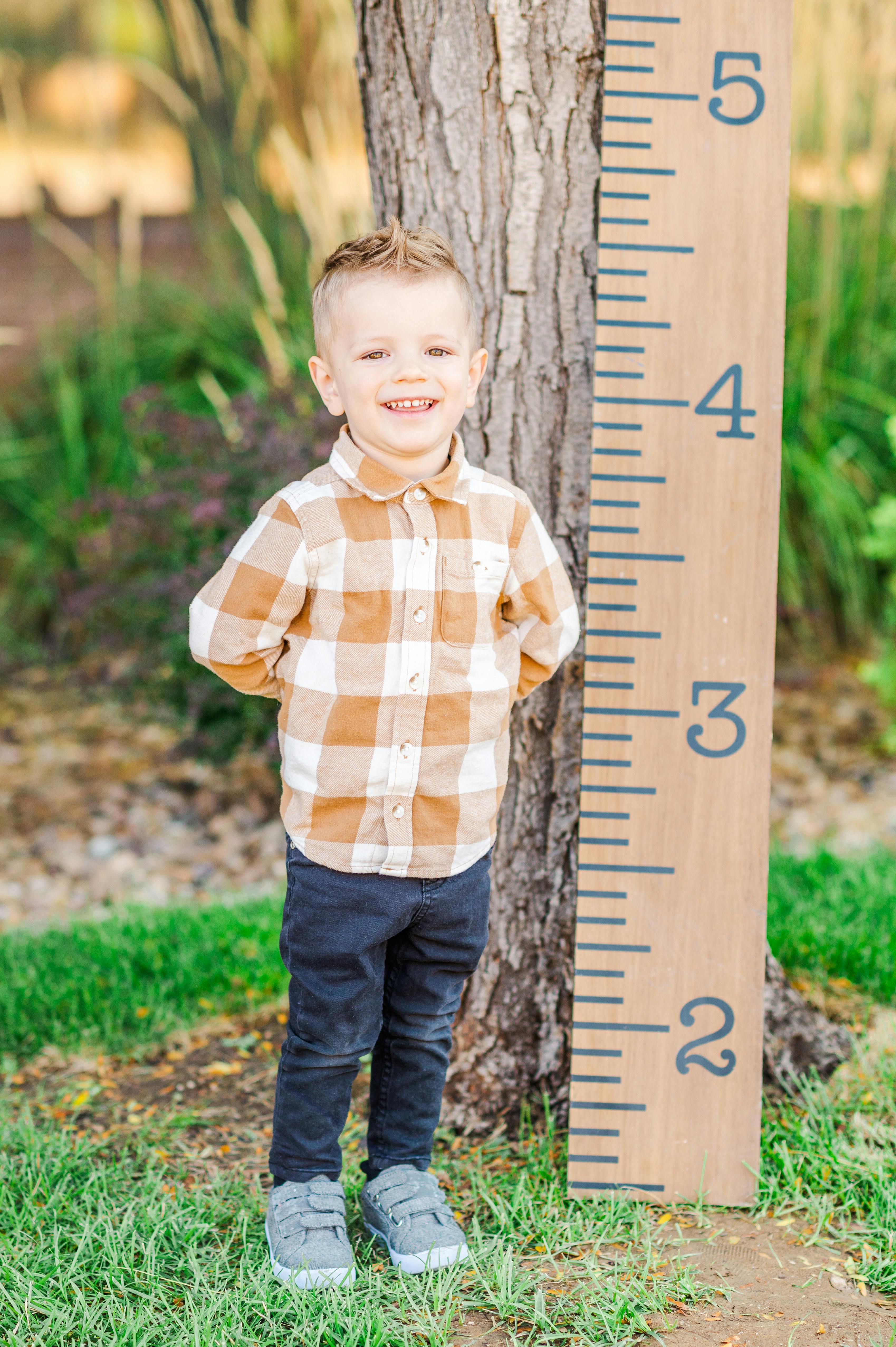 Child standing next to a wooden growth chart