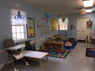 Empty classroom with small tables, chairs, and play mats