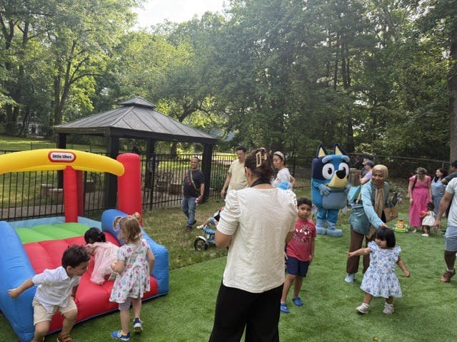 Children playing on an inflatable bounce house at a park with people nearby