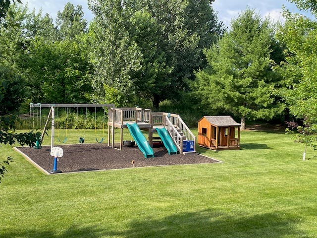 Outdoor playground with swings, slides, and a small playhouse on grass