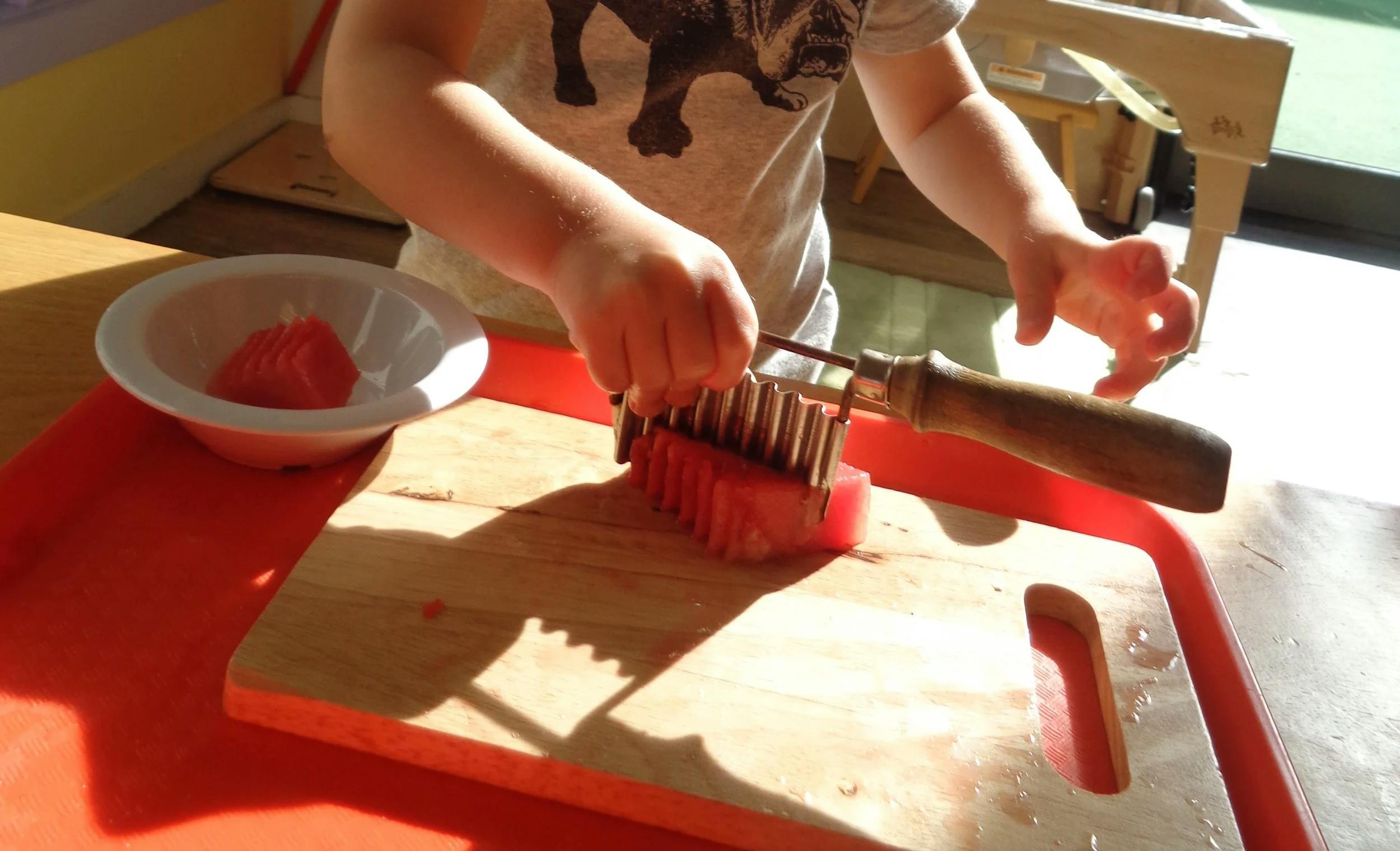 Child's hands holding a crinkle cutter over watermelon on a cutting board