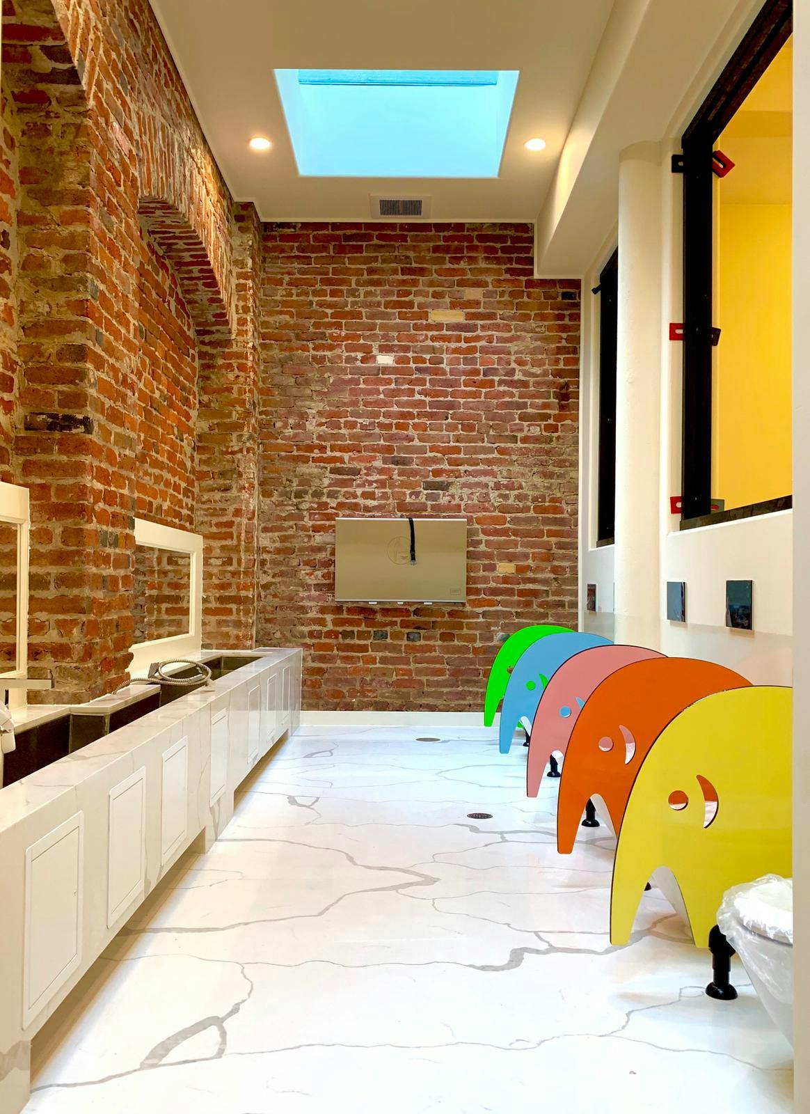 Hallway with brick walls, white cabinets, and colorful elephant-shaped chairs