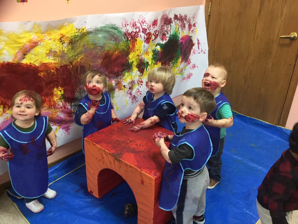 Children in aprons covered in paint standing around a table