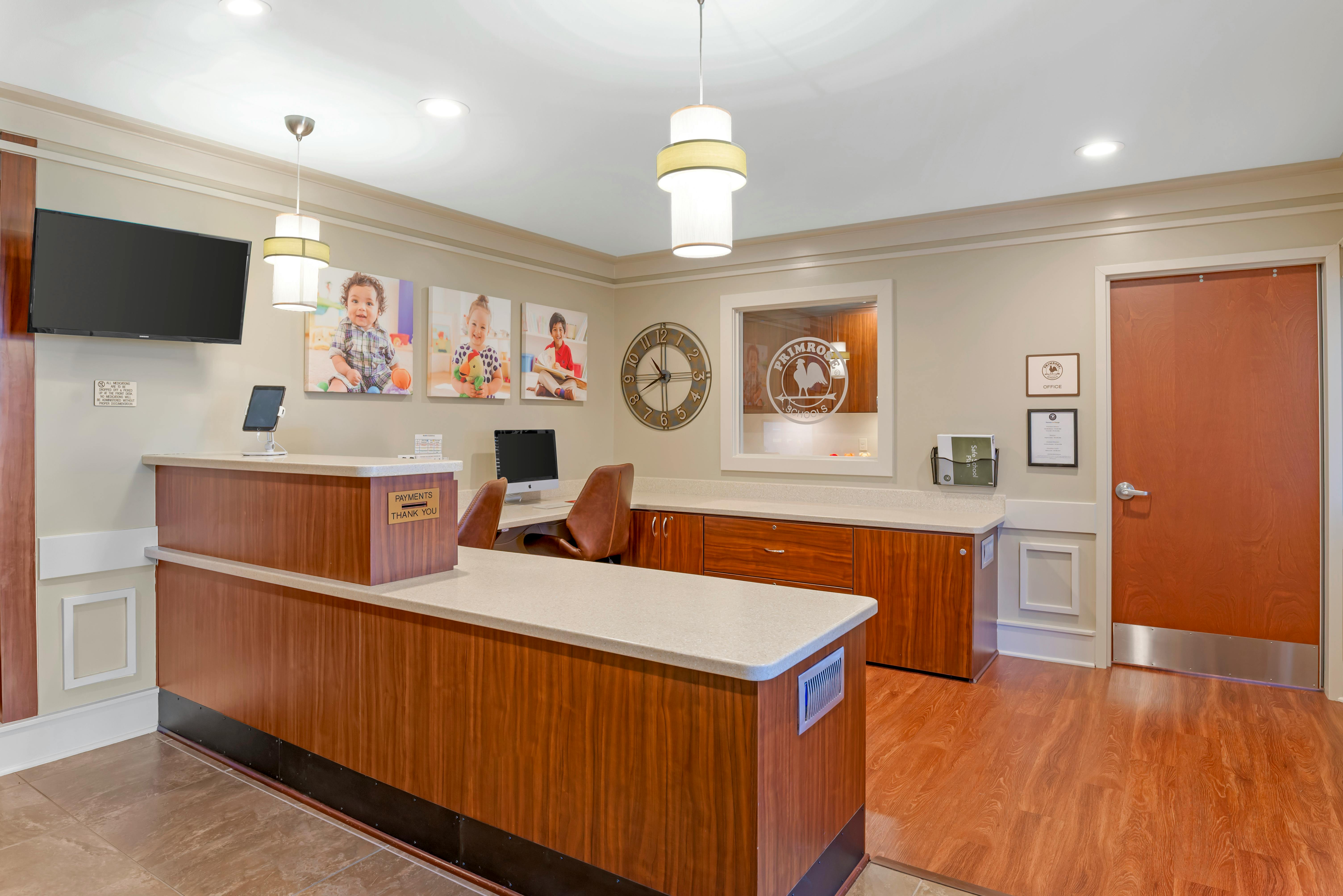 Reception area with a large wooden desk, wall-mounted screen, and photos of children