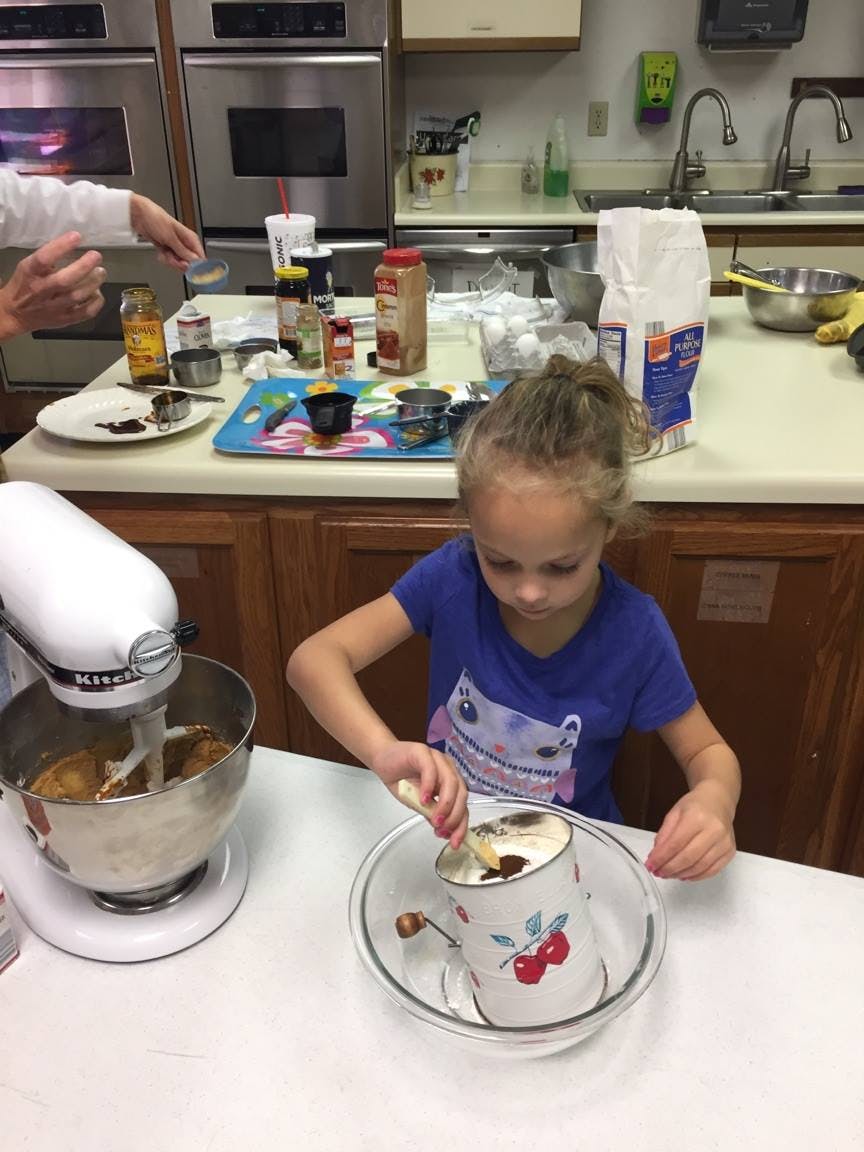 Child sifting ingredients into a bowl in a kitchen