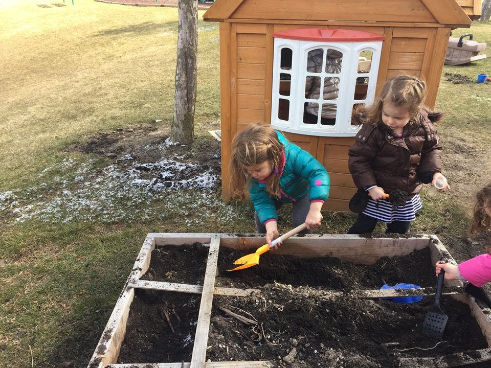 Child digging in a raised garden bed with a toy shovel