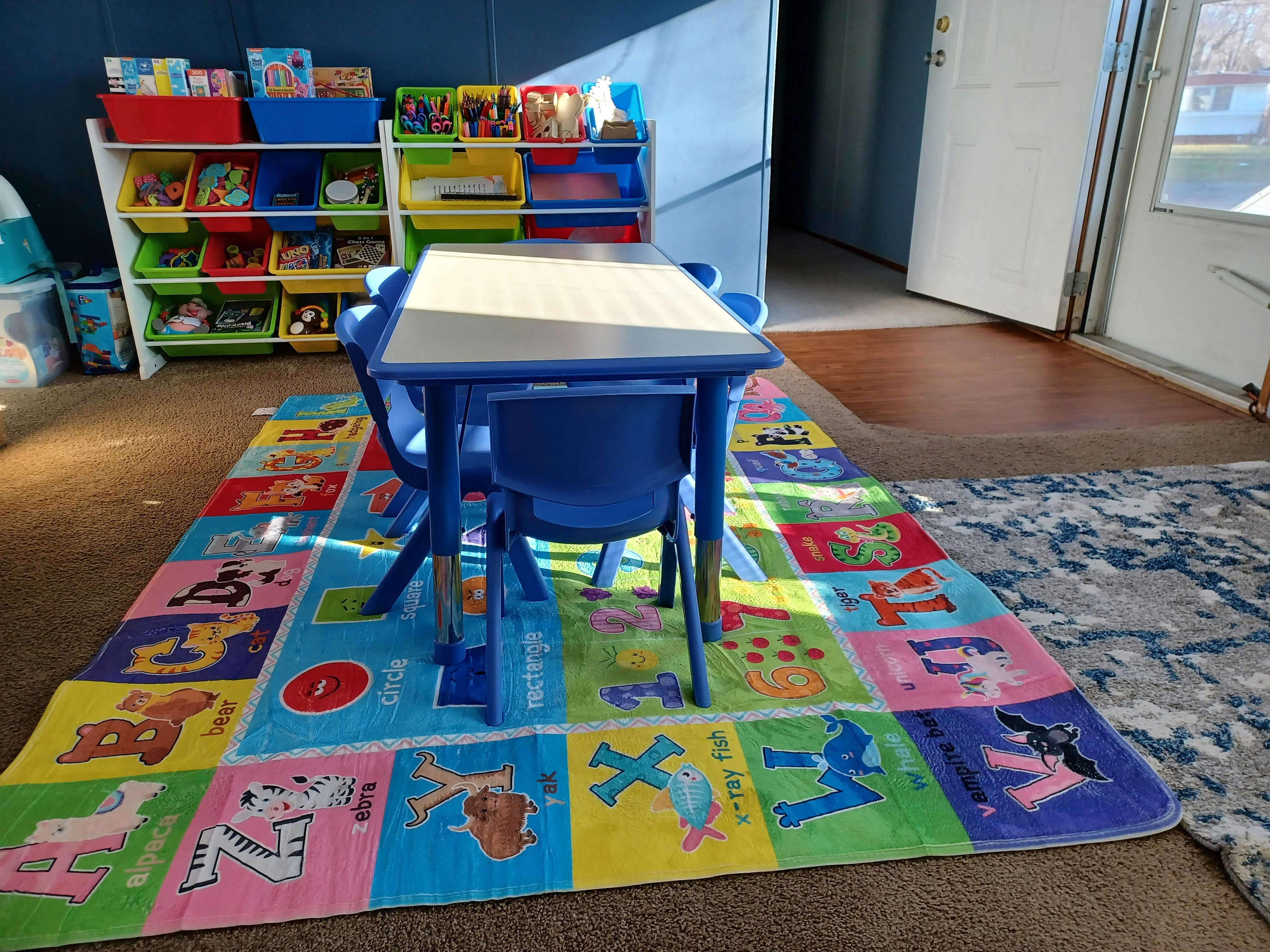 Child-sized table and chairs on an alphabet rug in a room with toy shelves
