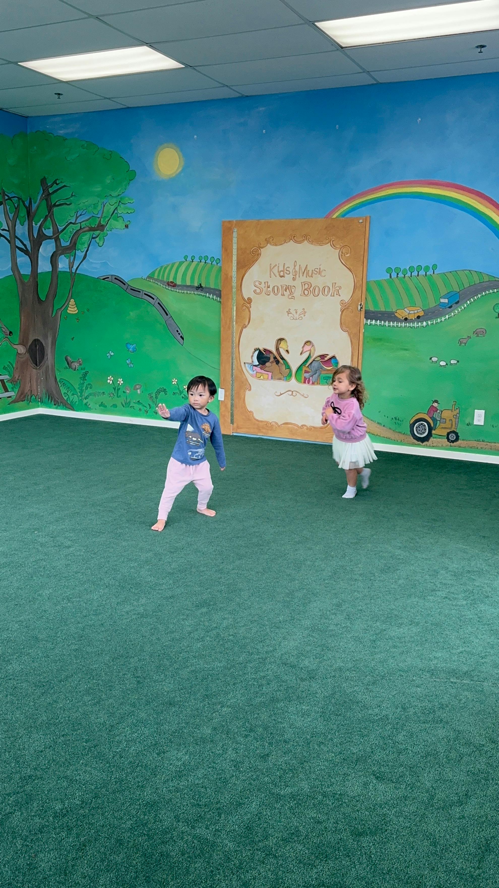 Two children playing in front of a painted storybook mural
