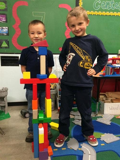 Two children standing next to a tall structure built from colorful blocks