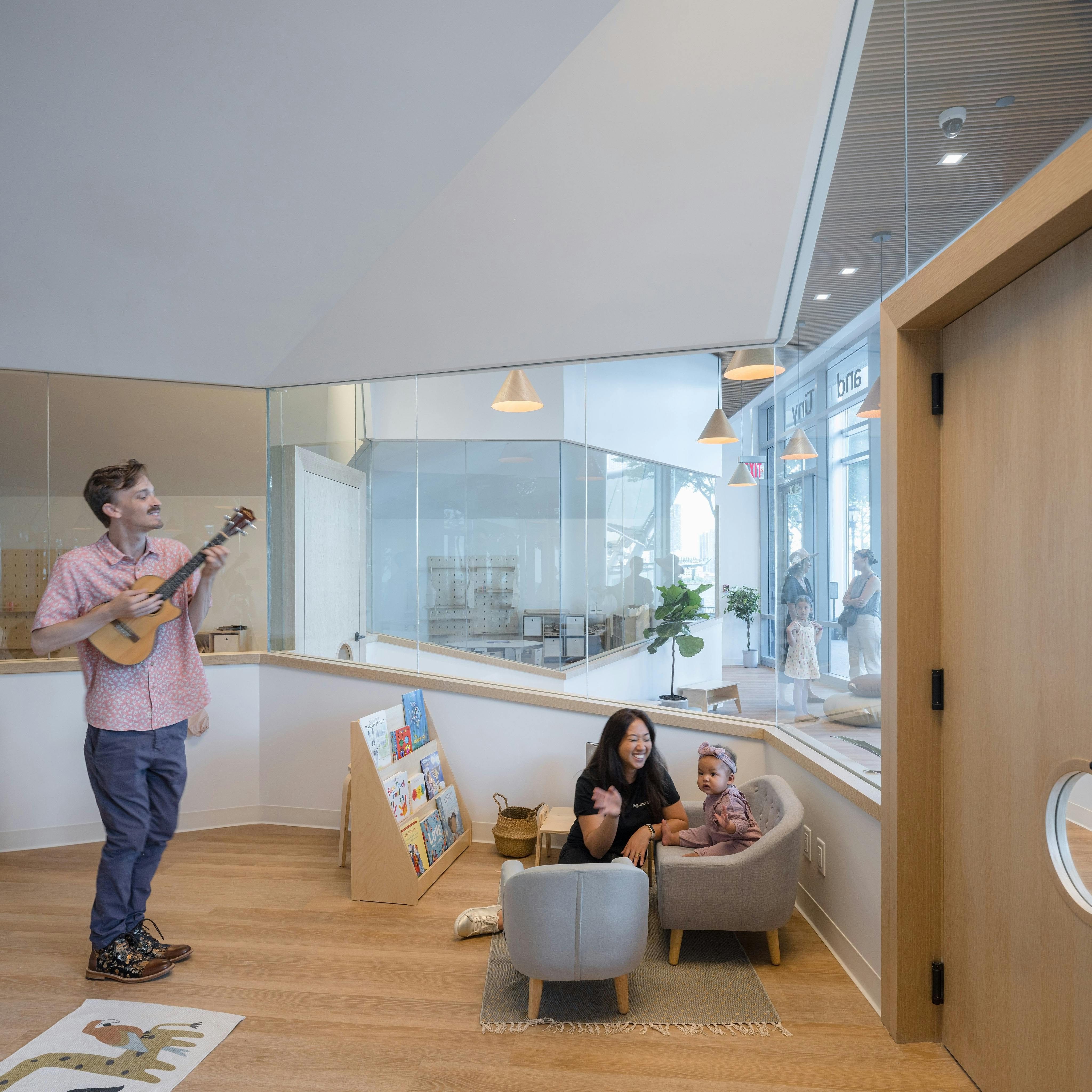 Person playing ukulele for a person and a child in a room