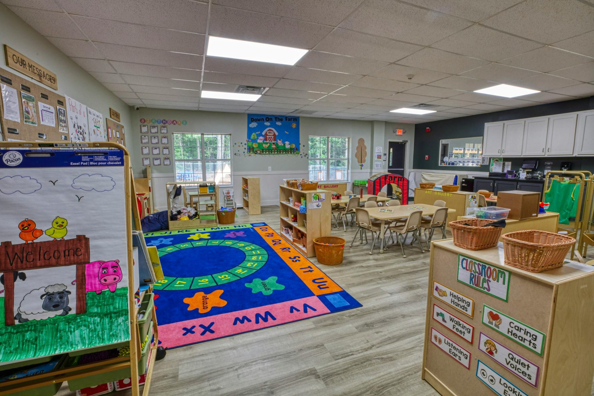 Classroom with small tables and chairs, a colorful rug, and a whiteboard