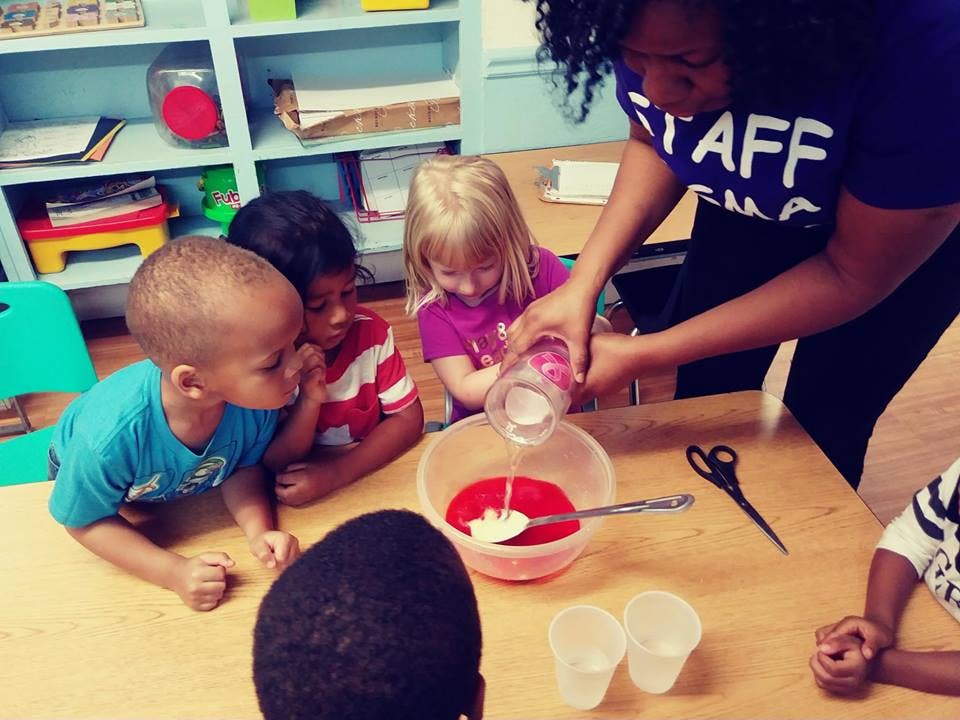 Adult pouring liquid into a bowl with children watching