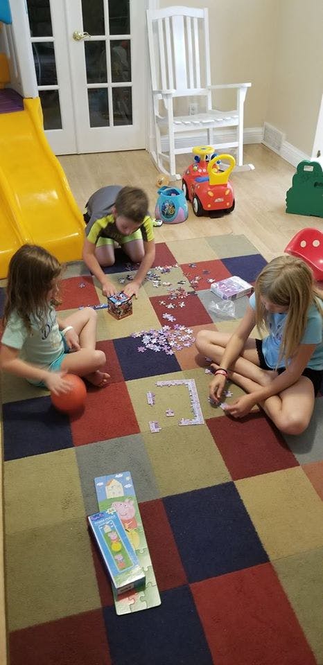Three children playing with puzzles on a checkered rug