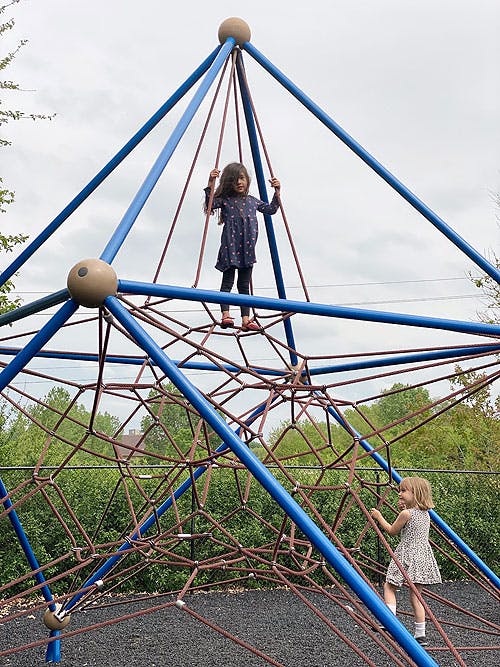 Two children climbing on a rope and pole playground structure