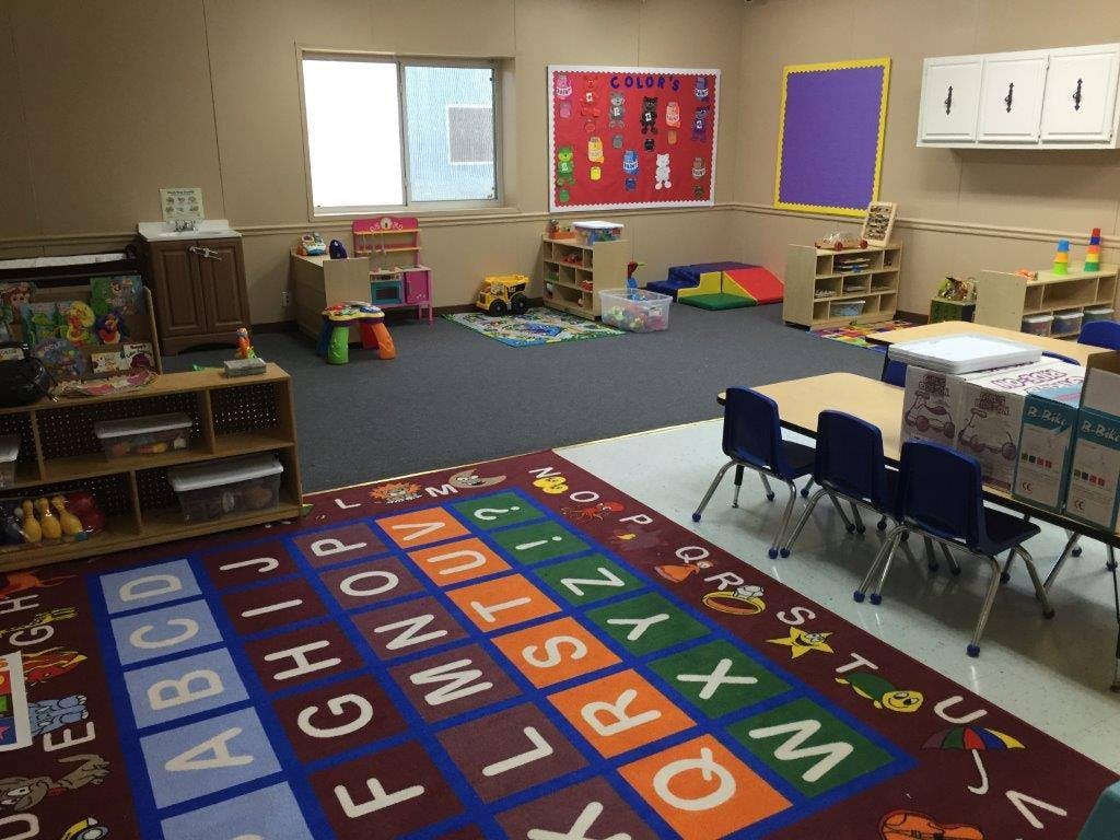 Empty classroom with an alphabet rug, small tables, and shelves