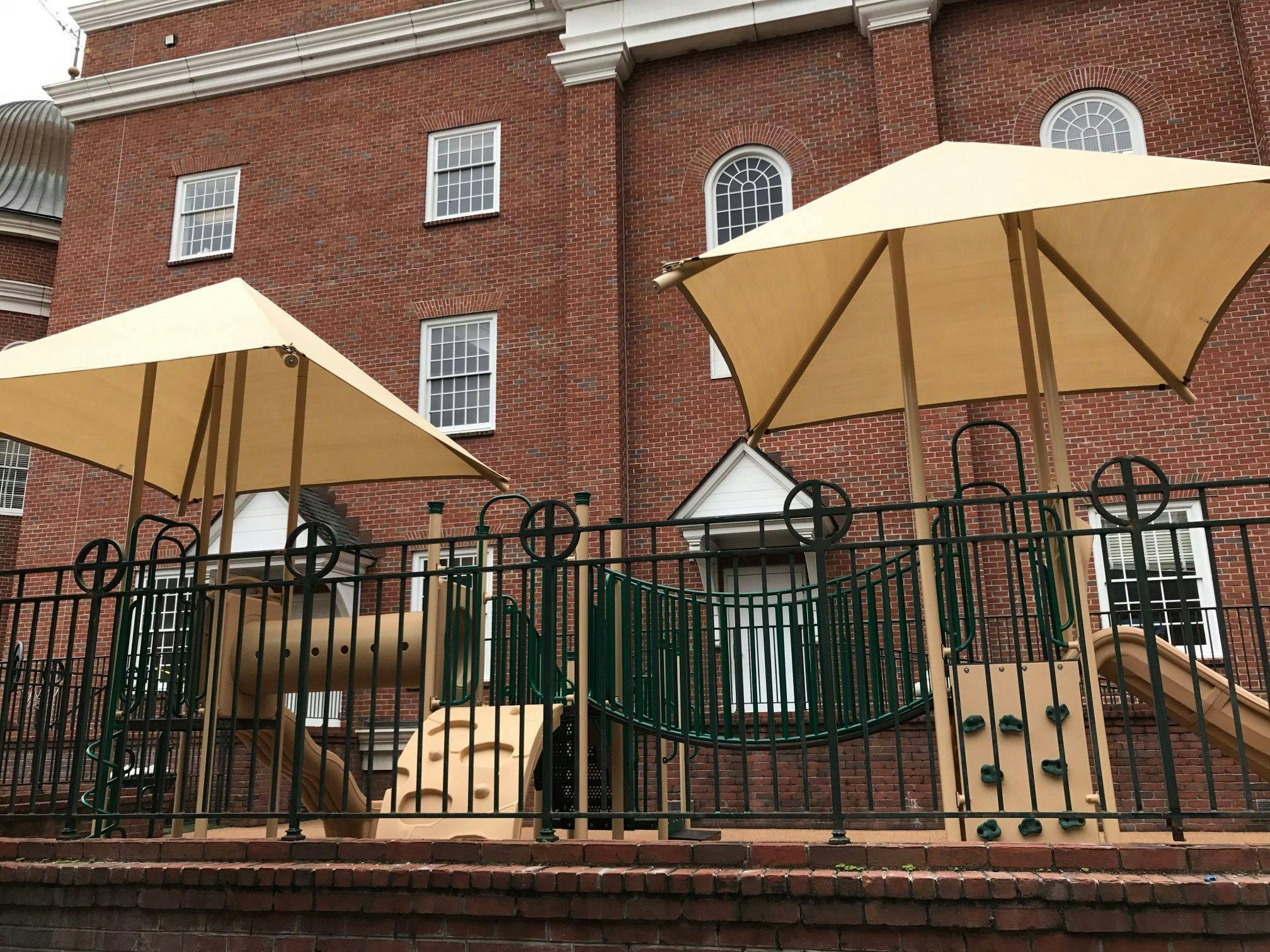 Playground with two large umbrellas in front of a brick building