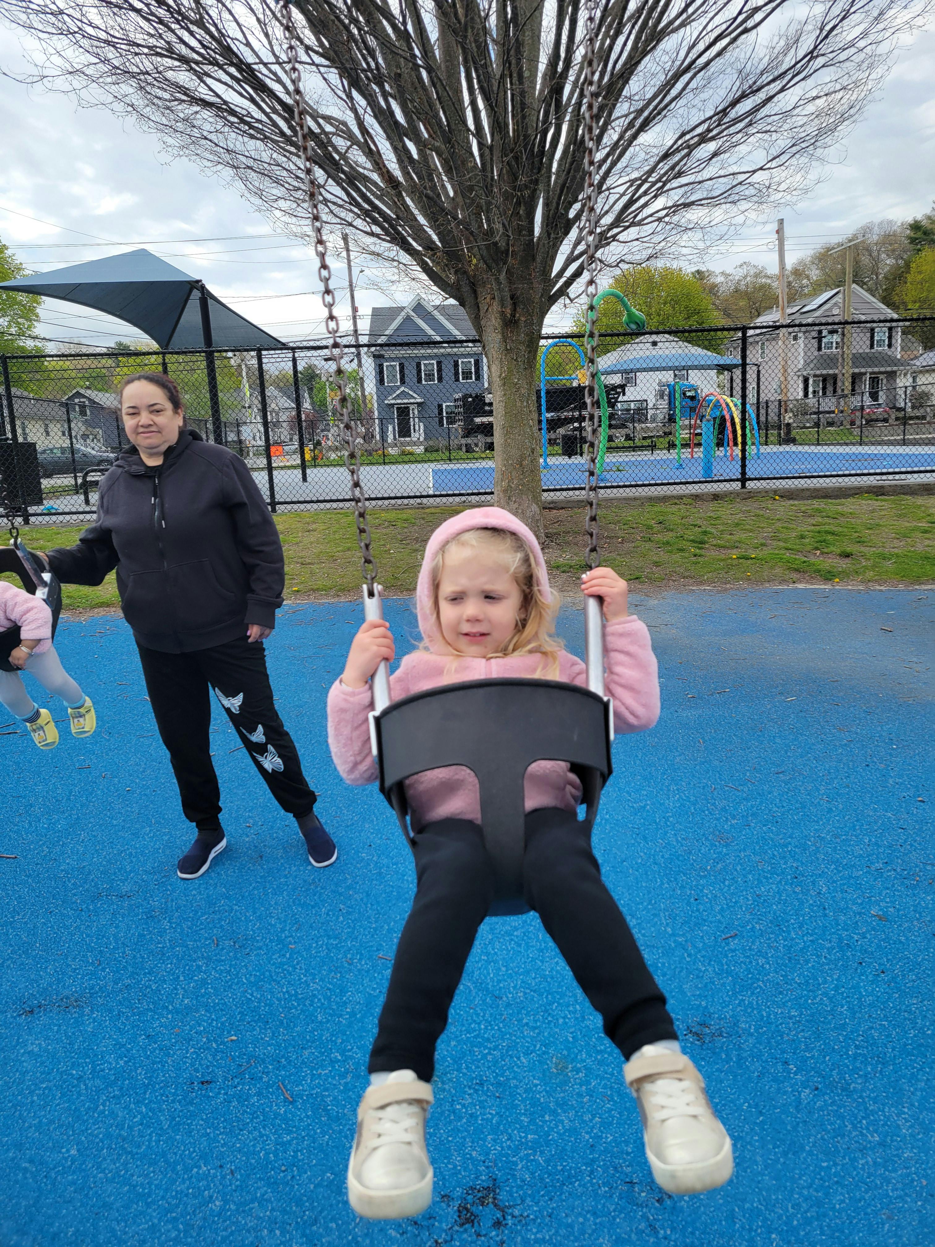 Child in a swing with a person standing nearby on a playground