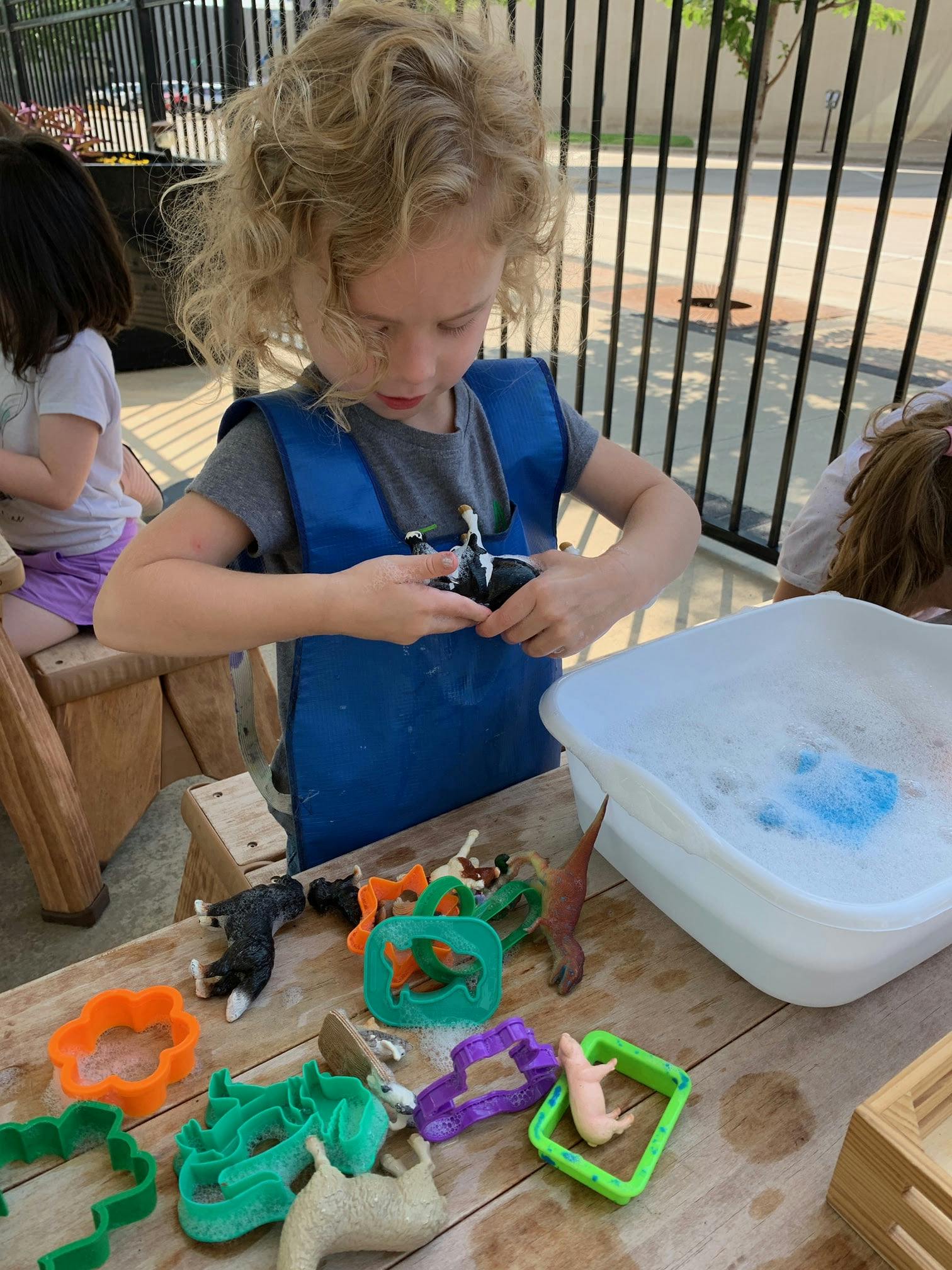 Child playing with small toys and cookie cutters next to a tub of soapy water