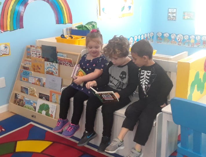Three children sitting and reading a book together in a classroom