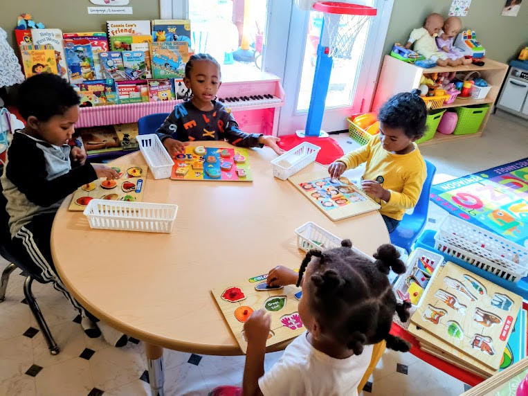 Four children playing with puzzles at a table in a classroom
