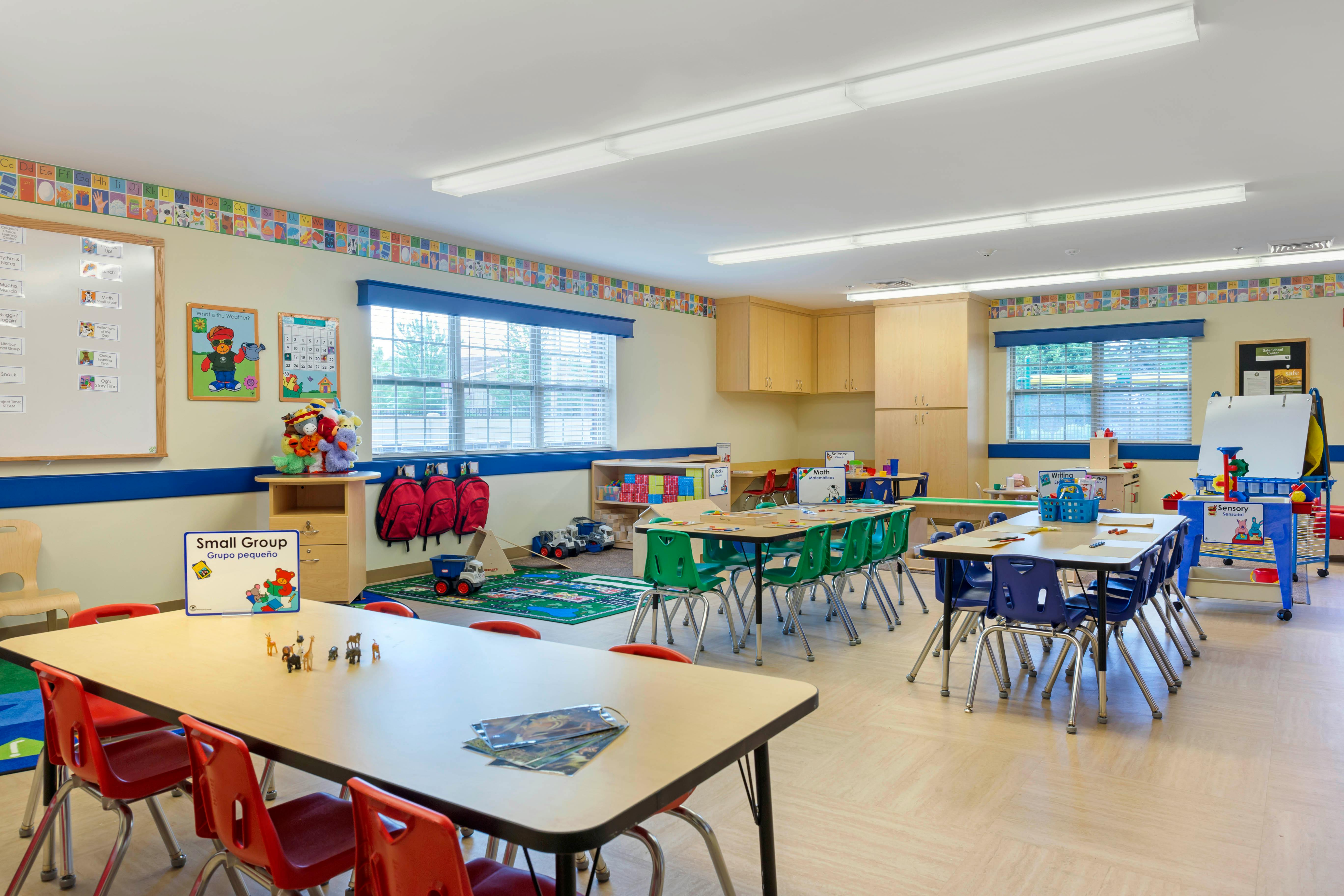Classroom with multiple tables and chairs, toys, and educational posters on the walls