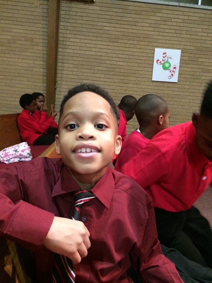 Child in a red shirt and striped tie looking forward