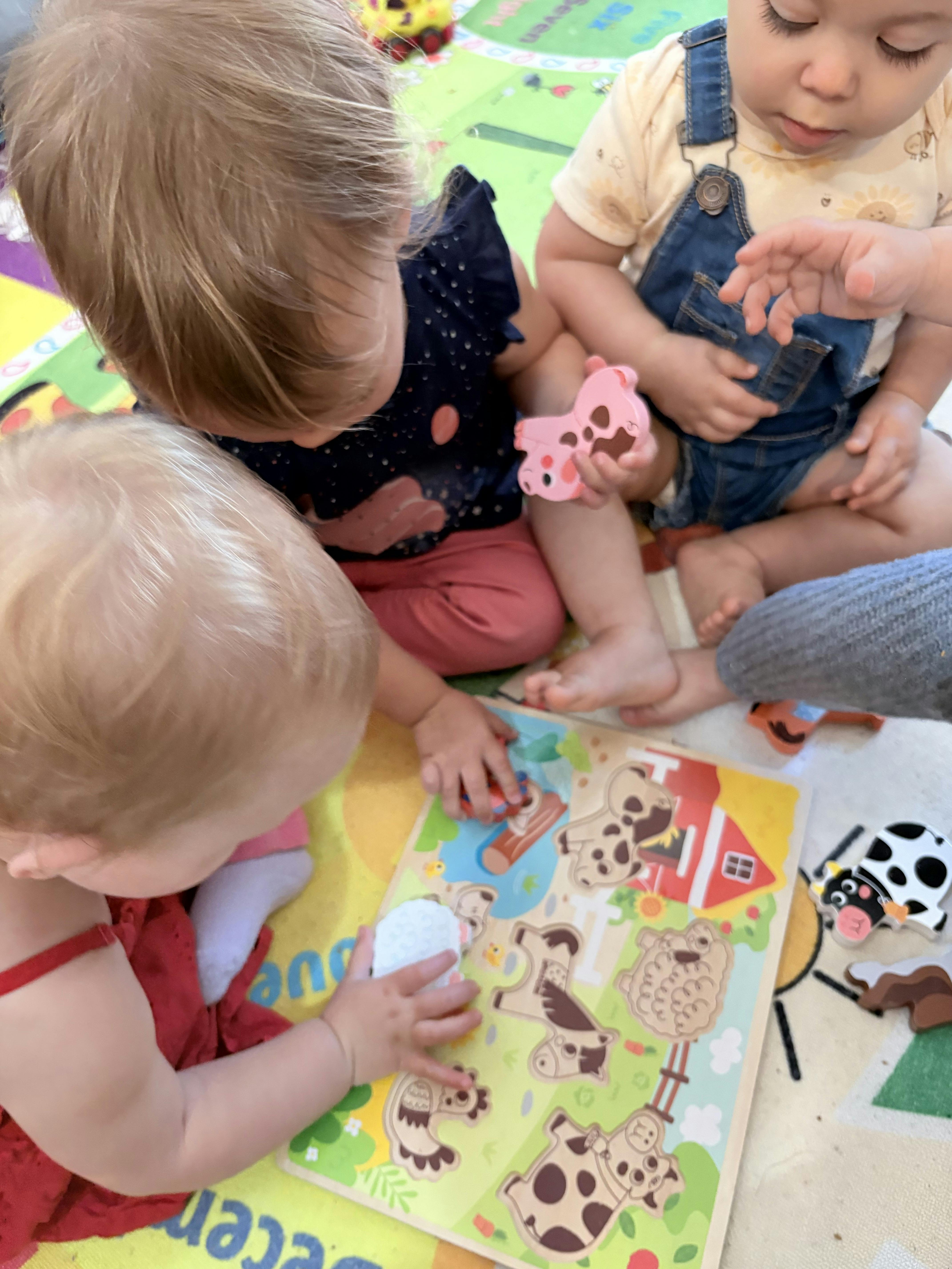 Three children playing with a farm animal wooden puzzle on a play mat