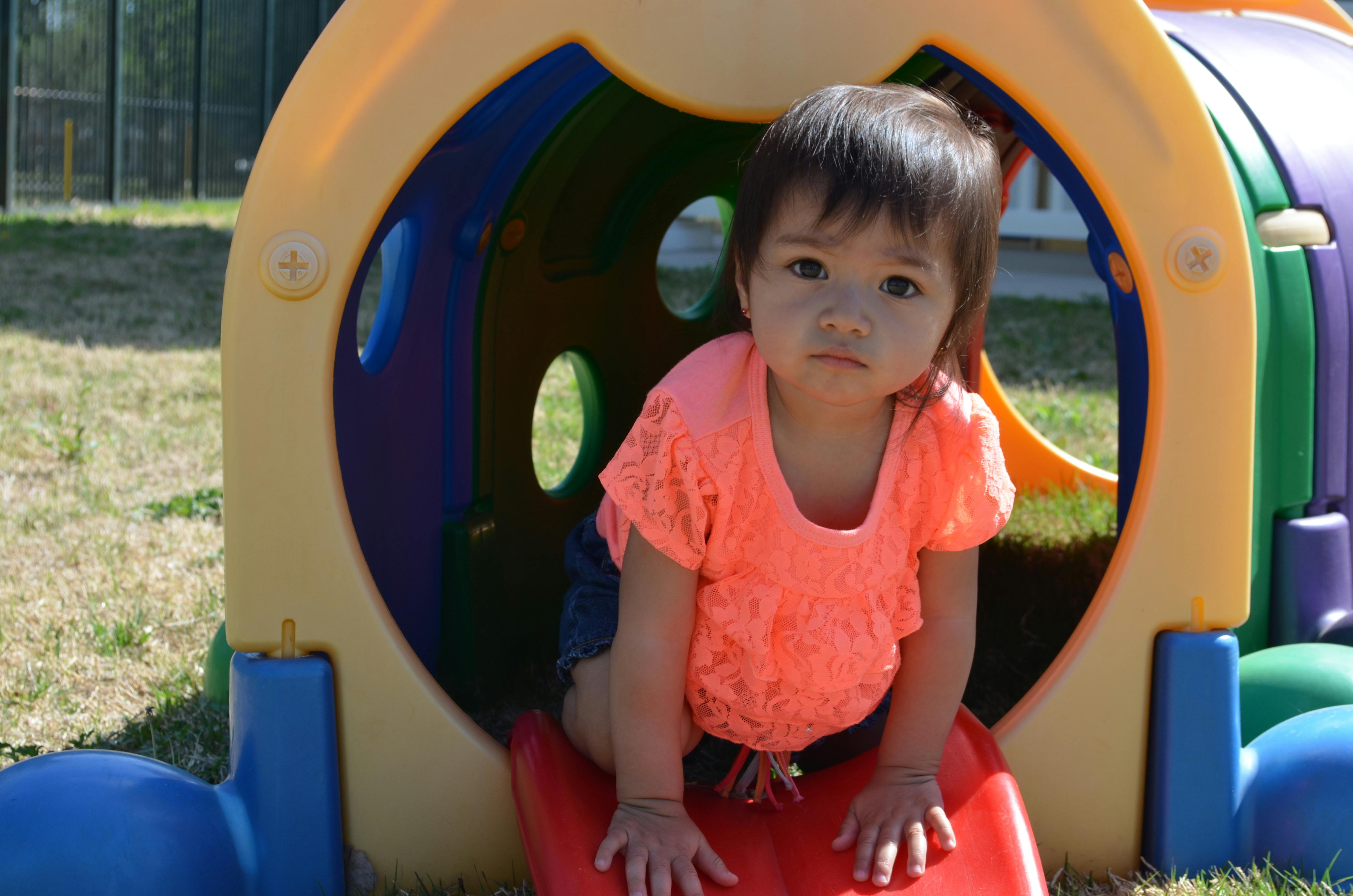 Child on a red slide coming out of a colorful play tunnel
