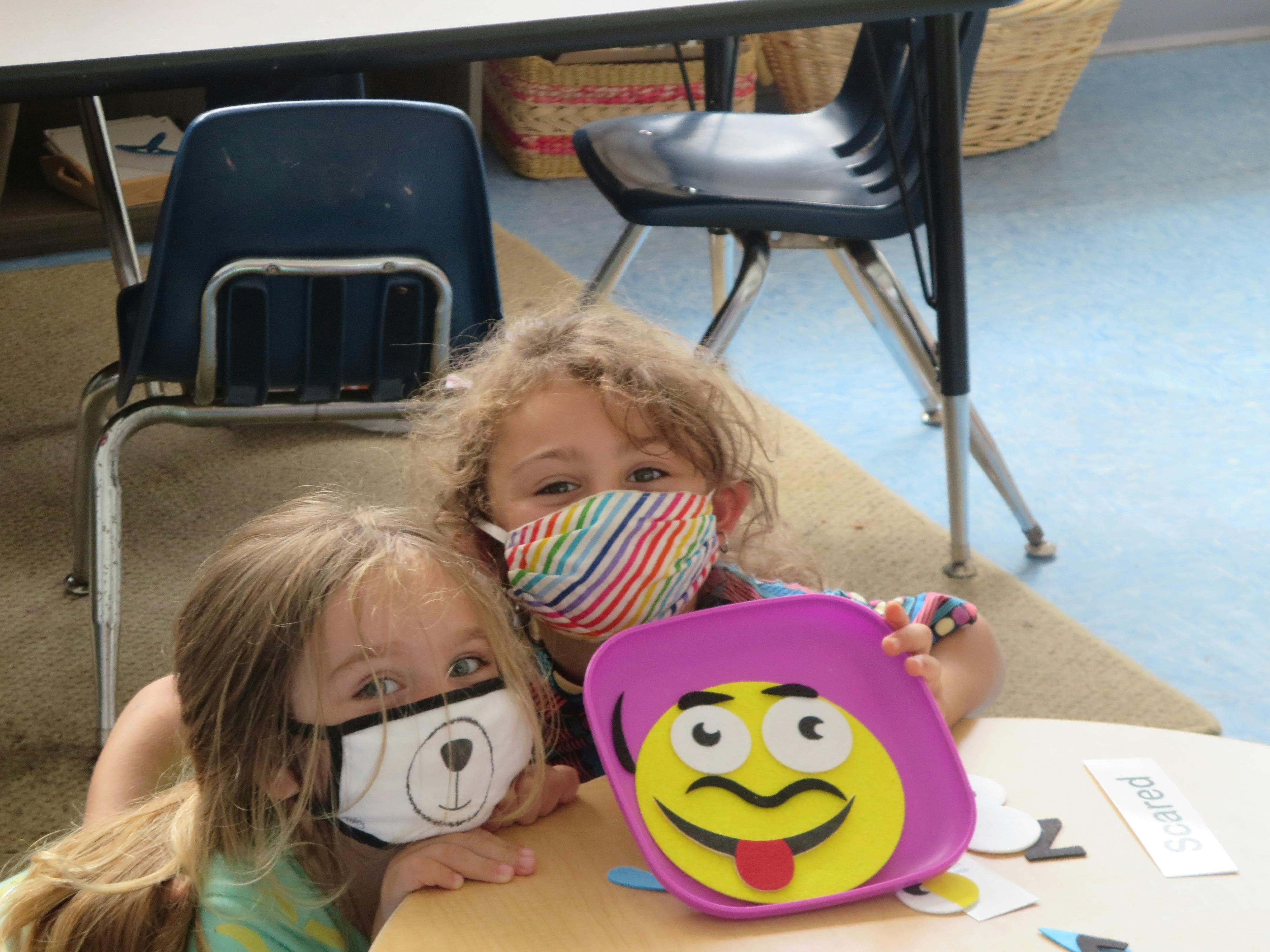 Two children in face masks looking at a purple plate with a cartoon face